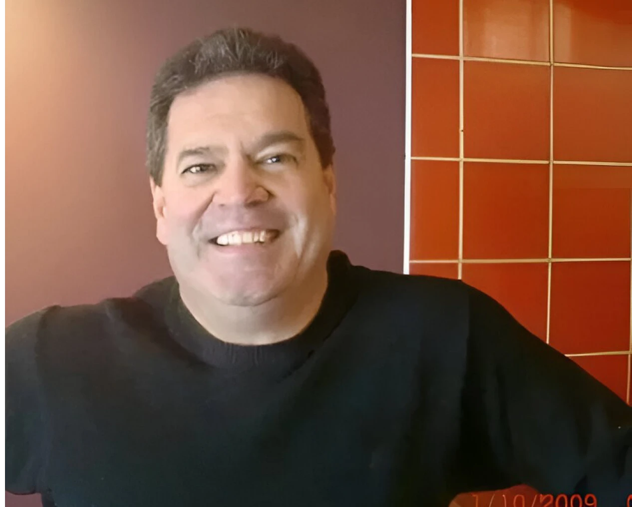 Smiling man in front of tiled wall.